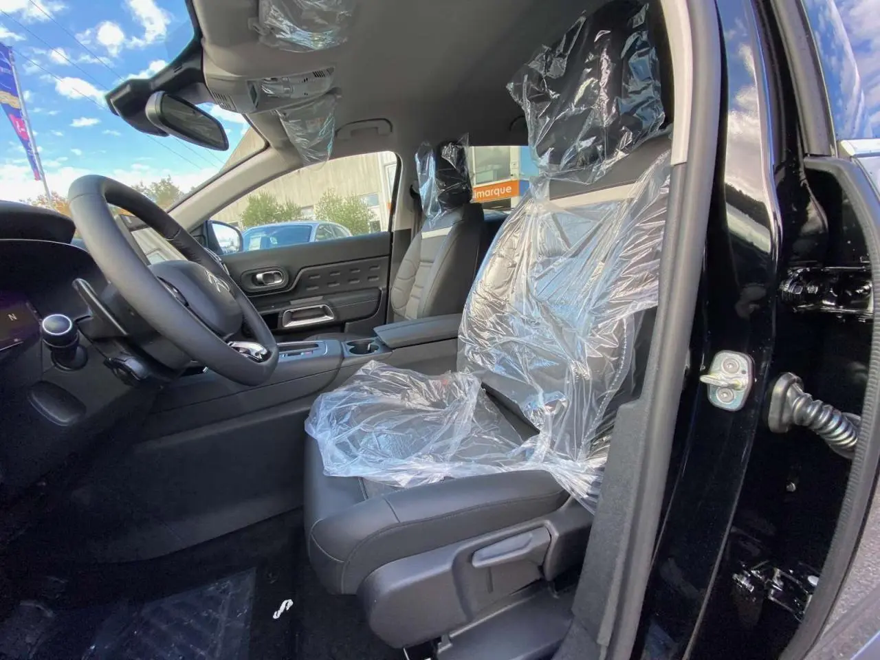 Intérieur avant du Citroën C5 Aircross noir Perla, sièges protégés par film plastique, volant et tableau de bord visibles.