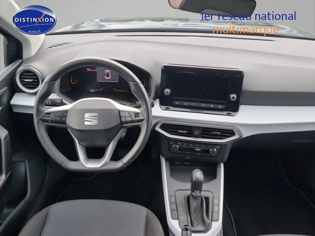 Vue intérieure frontale du tableau de bord gris clair et noir du SEAT Arona 2025 avec volant multifonction et écran tactile central.