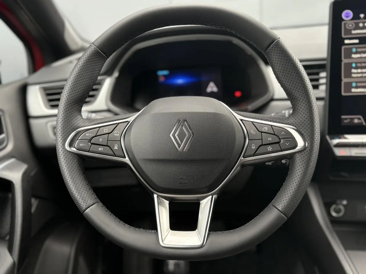 Vue rapprochée du volant en cuir noir perforé du Renault Captur 2025 avec commandes intégrées et tableau de bord numérique flou.