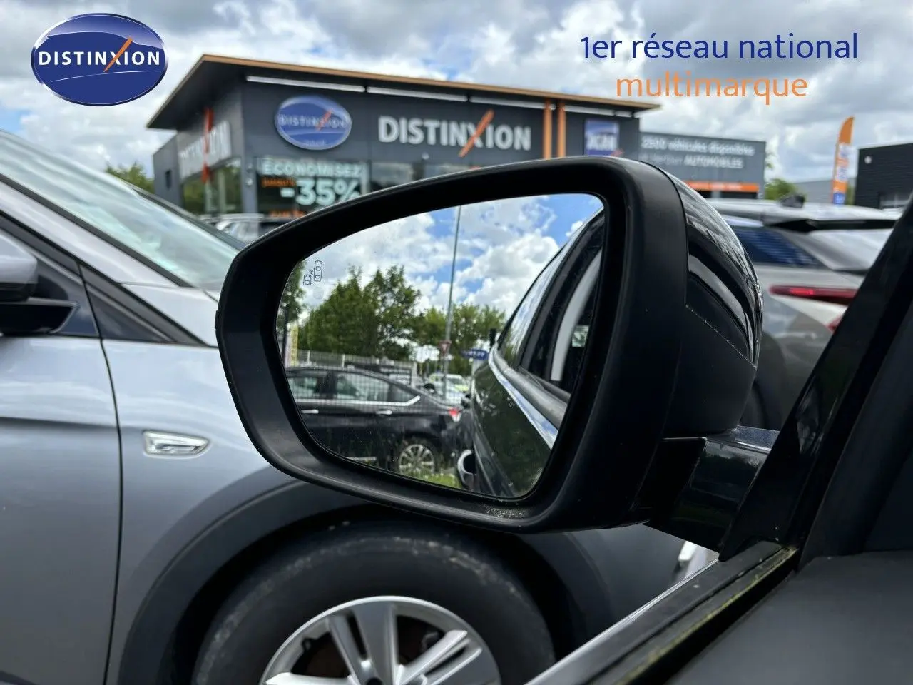 Rétroviseur côté gauche d’un Opel Grandland X noir, avec reflet sur un parking et bâtiment Distinxion en arrière-plan.