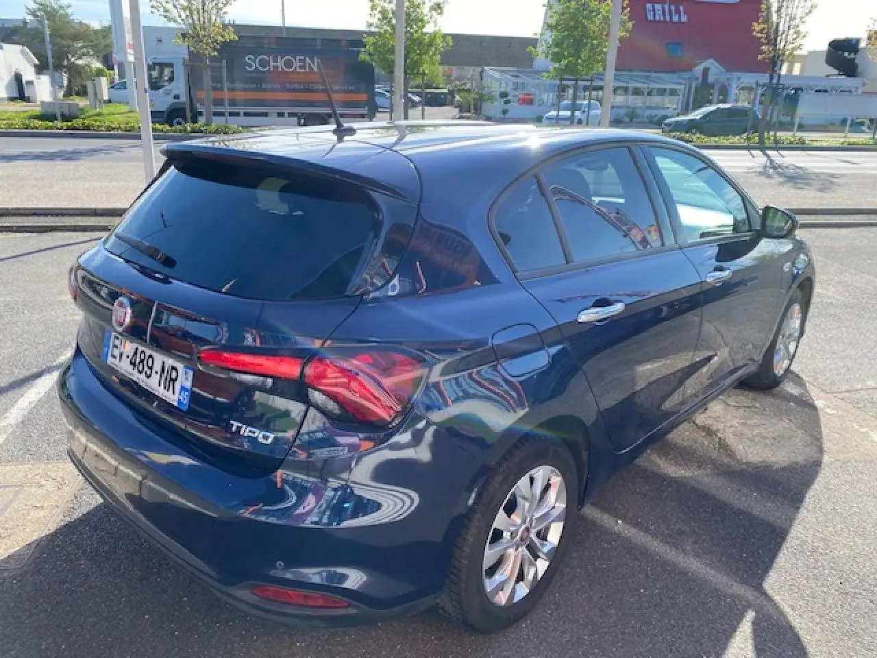 Vue 3/4 arrière droite d'une Fiat Tipo bleu métallisé avec vitres surteintées et feux arrière allumés.