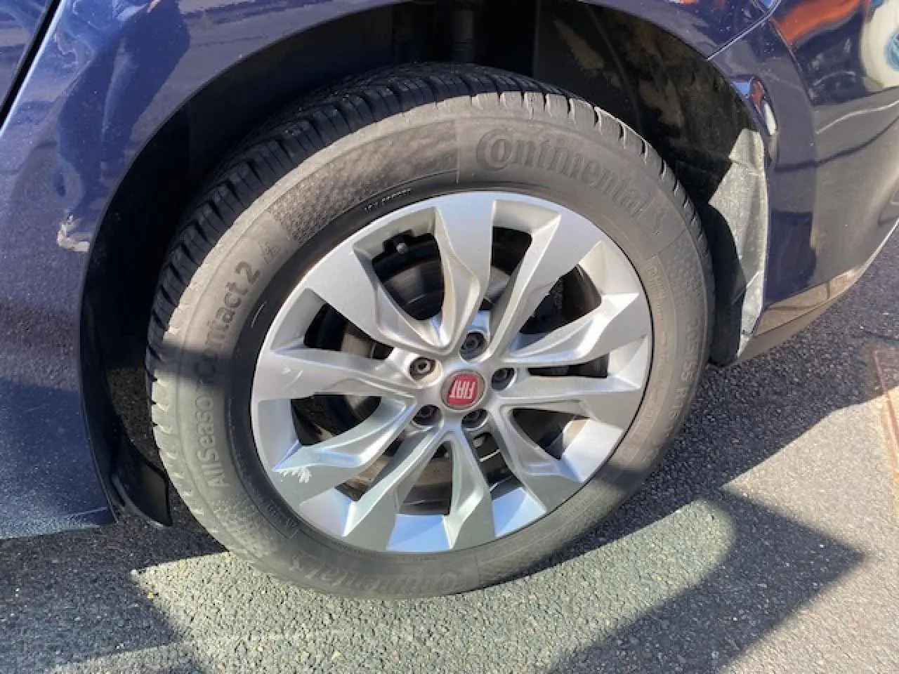 Gros plan sur la roue avant gauche d’une FIAT TIPO bleu métallisé avec jante argentée et logo rouge FIAT au centre.