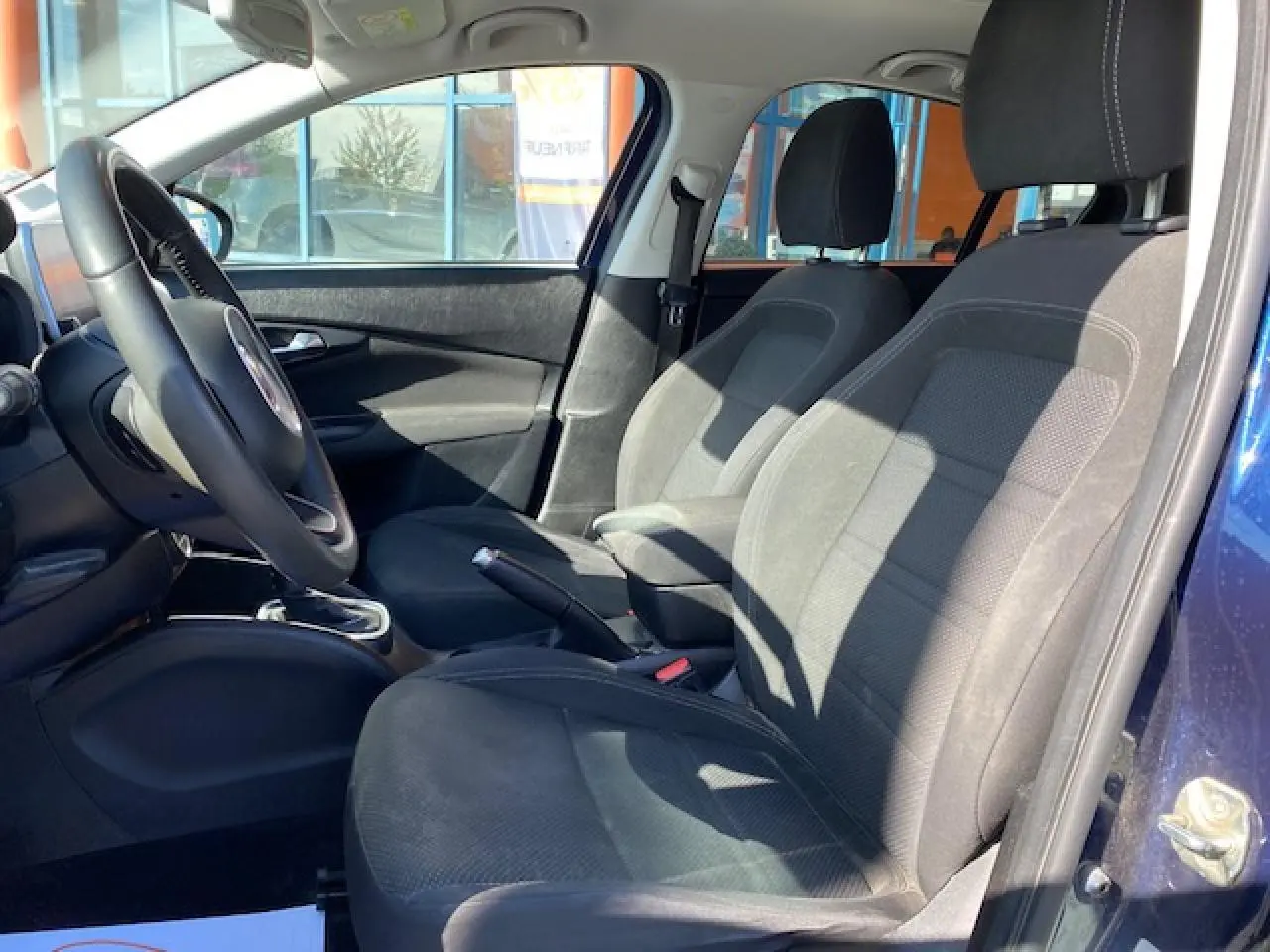 Vue intérieure côté conducteur de la Fiat Tipo bleu 2018, mettant en valeur les sièges tissu noirs et le volant.