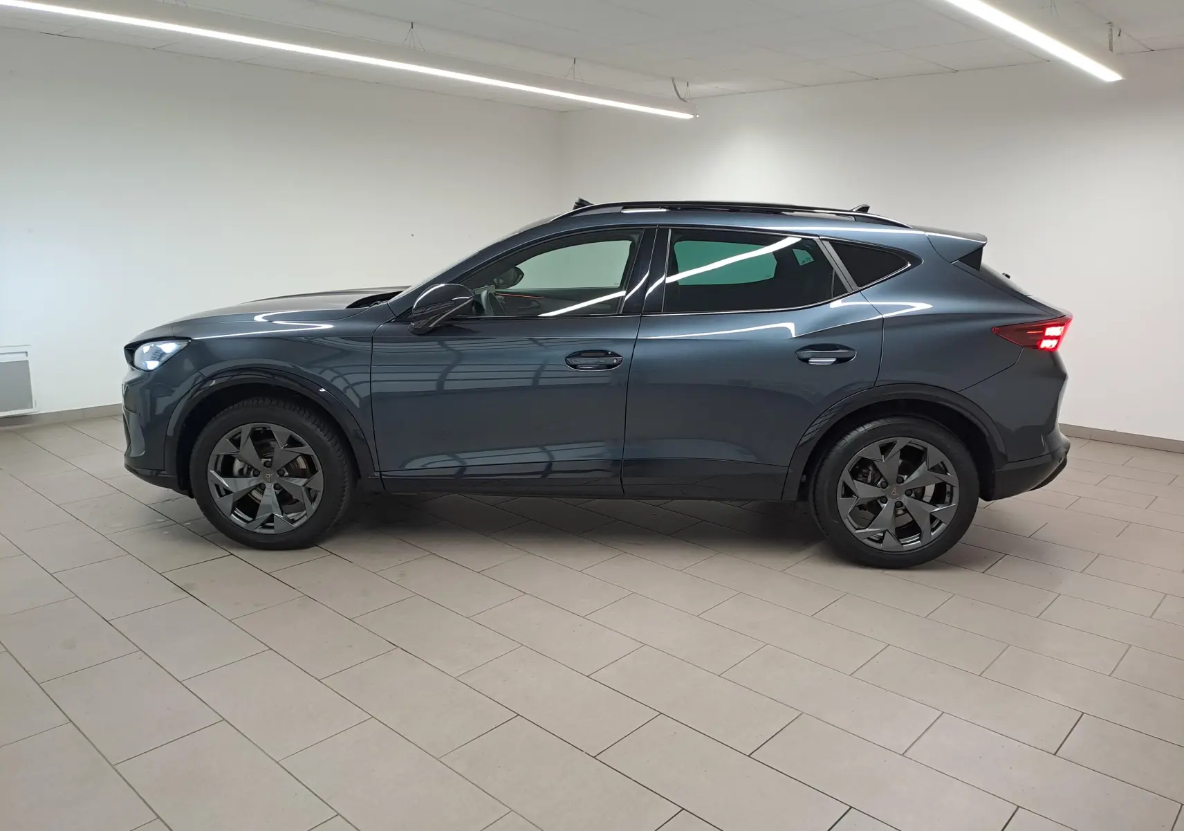 Vue de profil côté gauche du CUPRA Formentor gris magnétique 2025 avec jantes alliage noires et toit ouvrant panoramique.