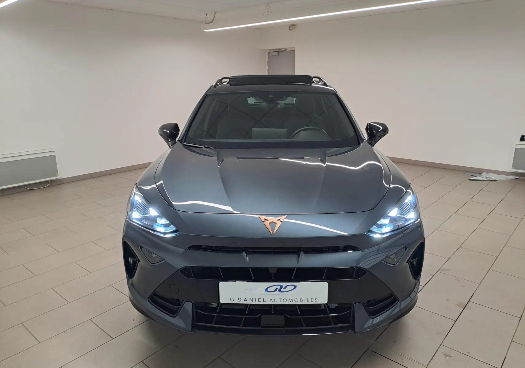 Vue frontale d'une CUPRA Formentor gris magnétique avec phares allumés et logo cuivré sur le capot.