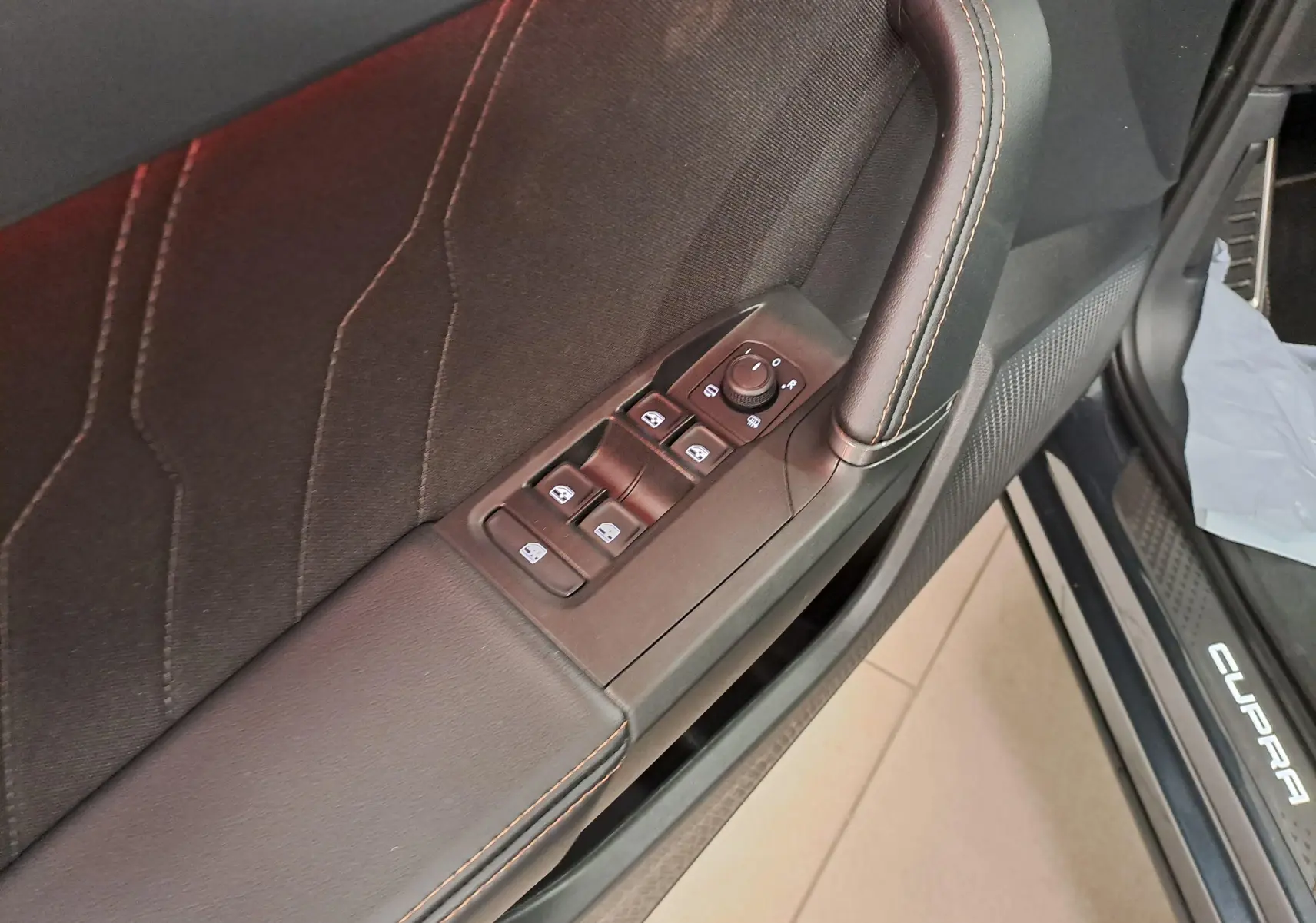 Détail de la porte côté conducteur du CUPRA Formentor gris magnétique, avec commandes des vitres et seuil de porte lumineux.