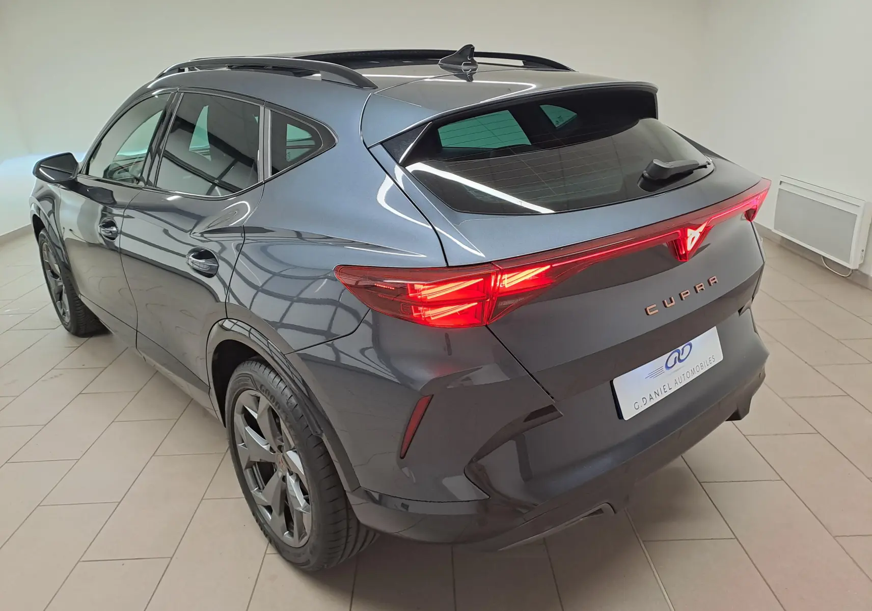 Vue 3/4 arrière droite du CUPRA Formentor gris magnétique avec feux arrière lumineux et toit ouvrant panoramique visible.