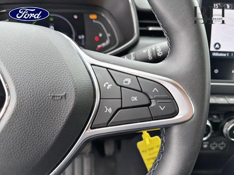 Gros plan sur les commandes au volant côté droit d’un Renault Clio blanc, avec écran tactile en arrière-plan.