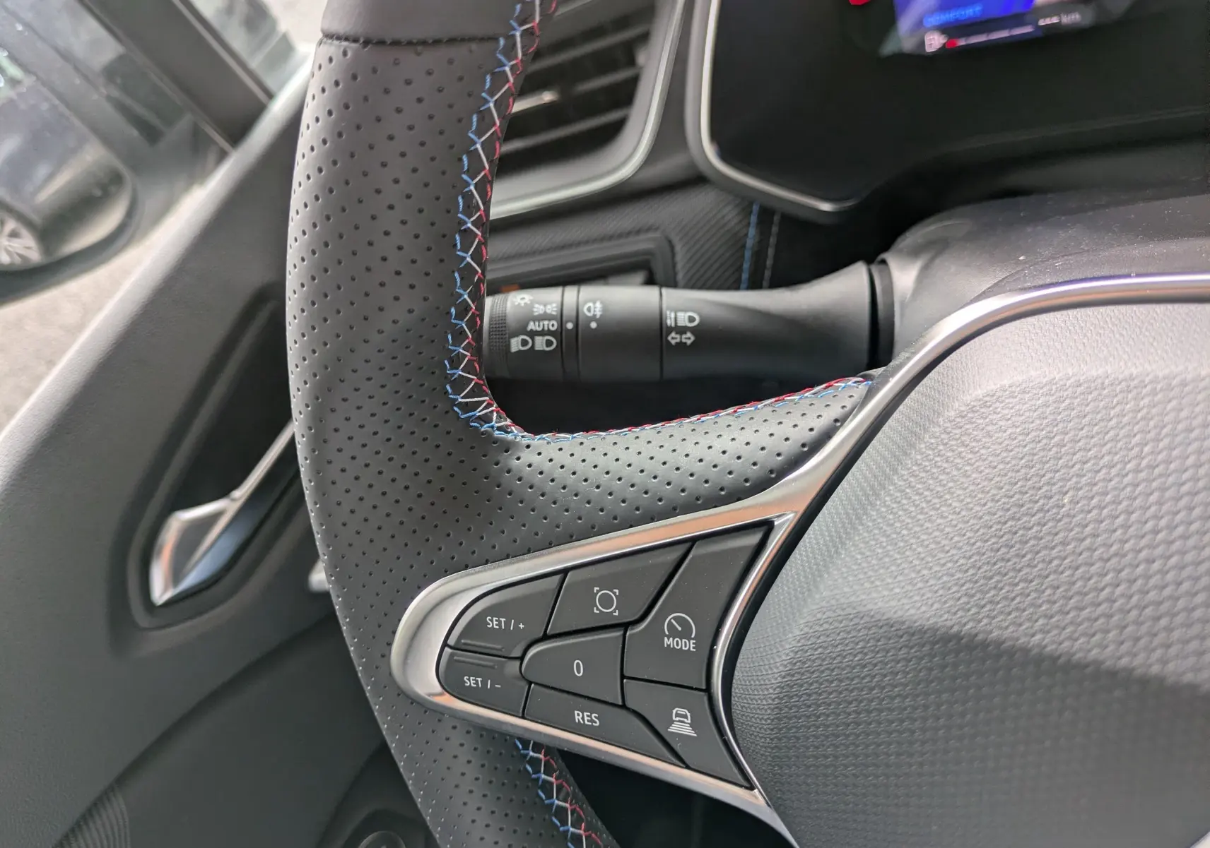 Gros plan sur le volant perforé avec surpiqûres tricolores du Renault Symbioz, montrant les commandes intégrées côté gauche.