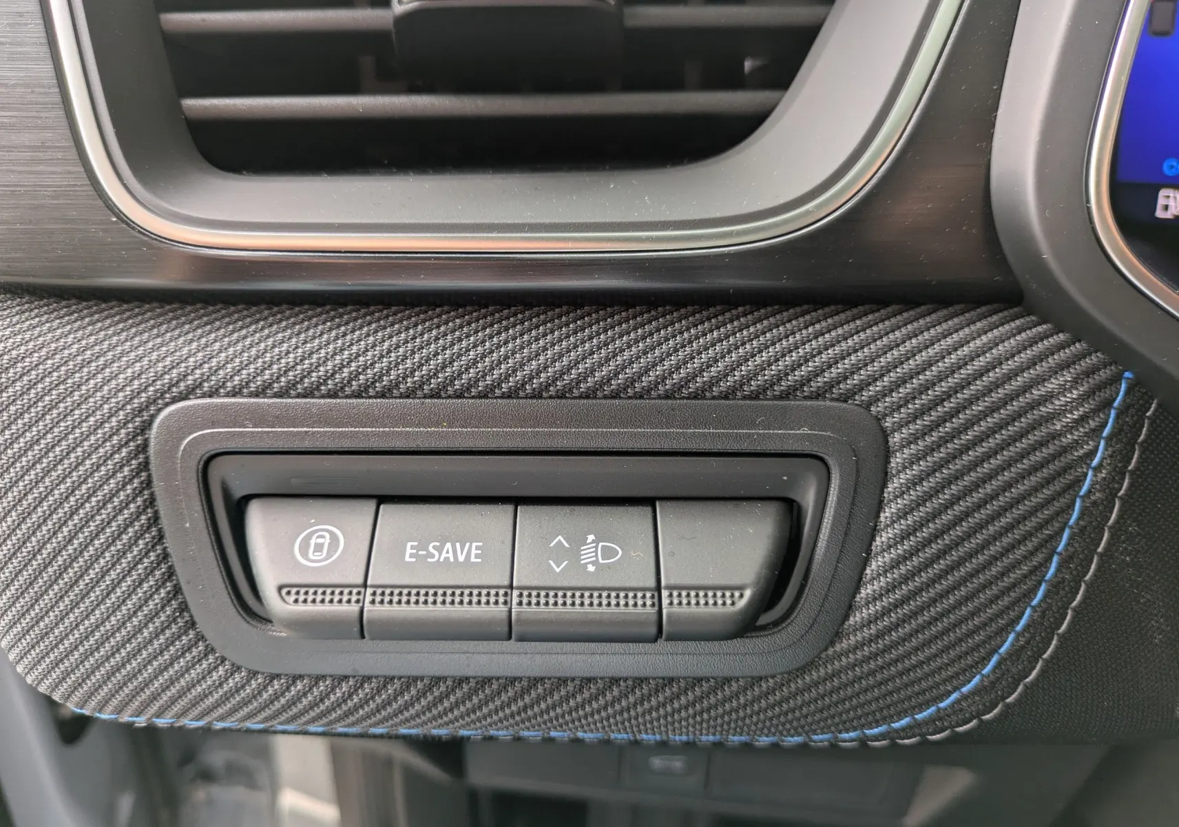 Détail des commandes E-SAVE et réglage des phares sur la planche de bord en tissu gris avec surpiqûres bleues du Renault Symbioz 2026.