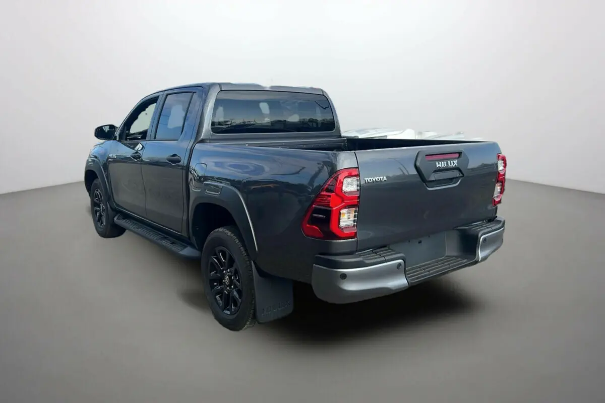 Toyota Hilux 4x4 gris atlas vue 3/4 arrière droit, avec benne ouverte et jantes noires distinctives.