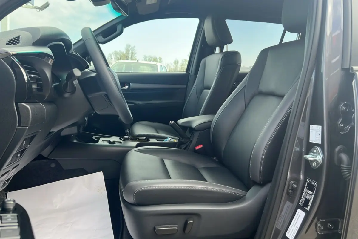 Intérieur du Toyota Hilux 2025 gris atlas, vue côté conducteur ouverte, sièges avant en cuir noir avec coutures blanches.
