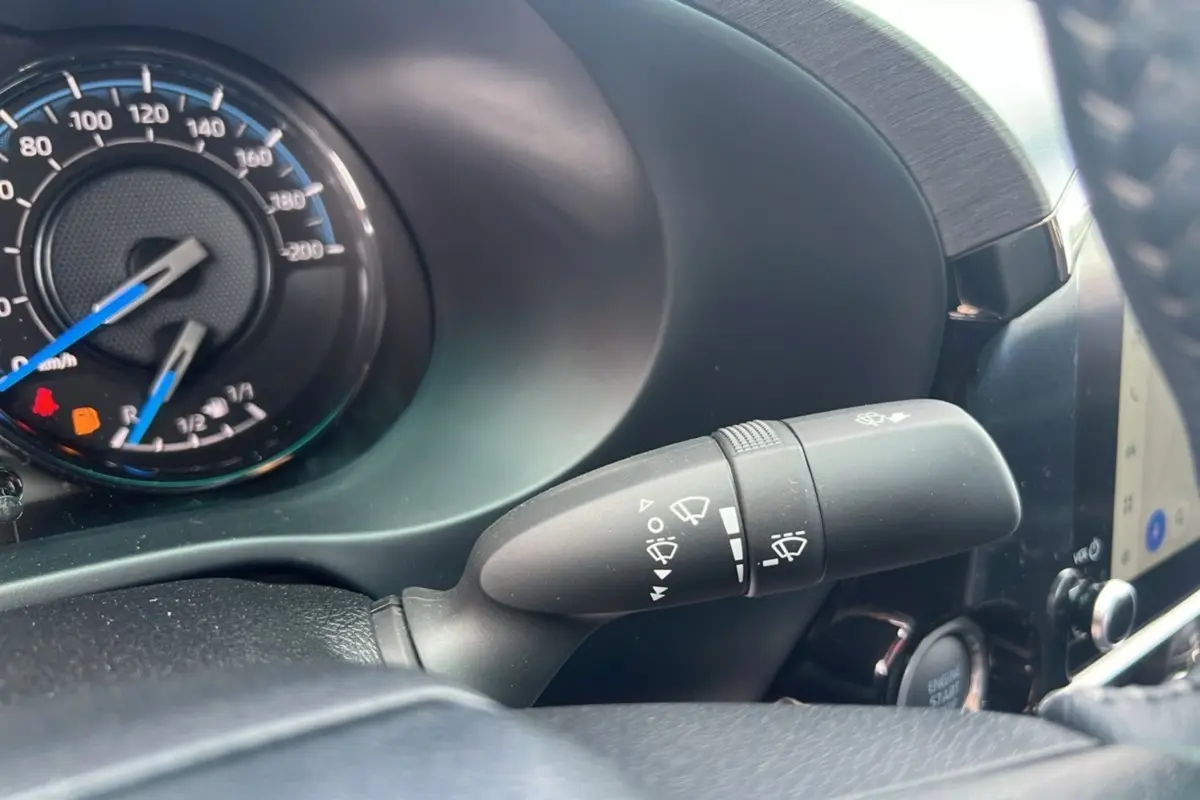 Gros plan sur la commande d'essuie-glace du Toyota Hilux 2025 gris atlas, avec tableau de bord et bouton démarrage visibles.