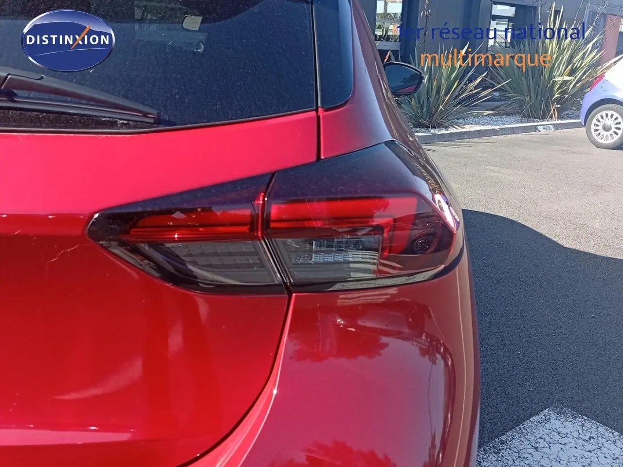 Vue arrière droite d'une Opel Corsa rouge métal avec toit noir, mettant en valeur le feu arrière moderne et la carrosserie brillante.