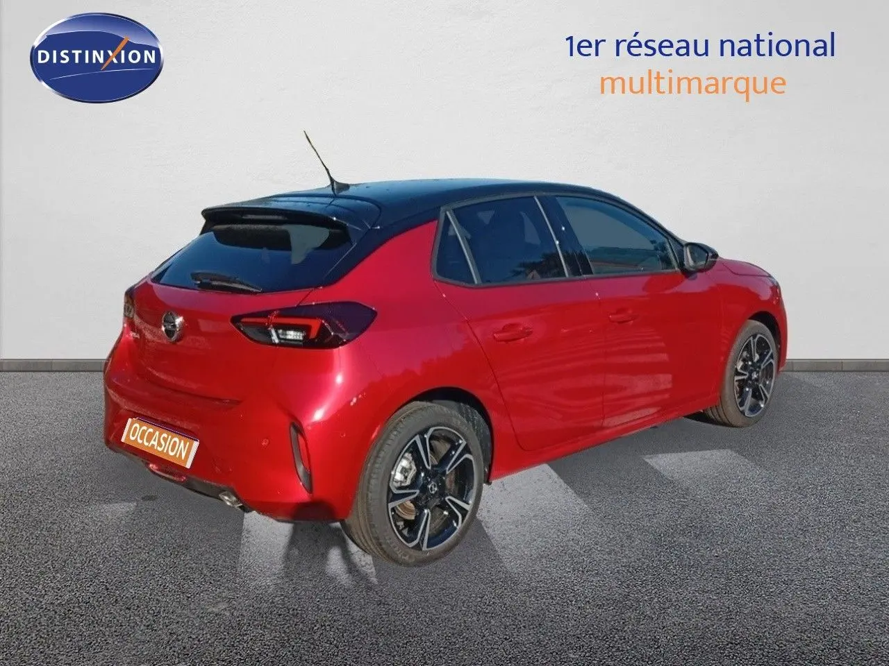 Vue 3/4 arrière droite d’une Opel Corsa rouge métal avec toit noir et jantes alliage noires, en extérieur sur sol gris.