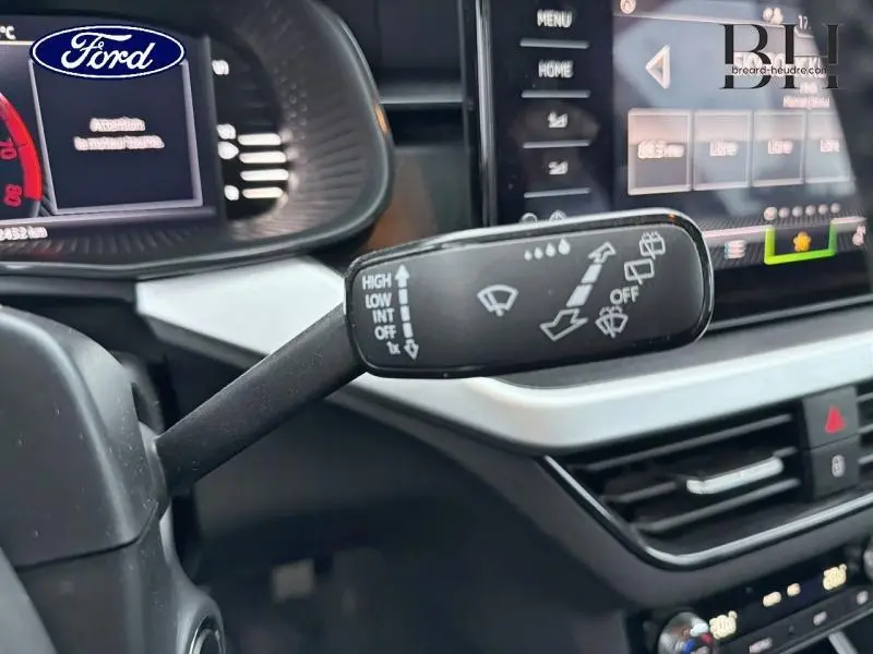 Le levier de commande des essuie-glaces en gros plan dans l'habitacle d'une Skoda Kamiq gris Météore, avec tableau de bord et écran tactile en arrière-plan.