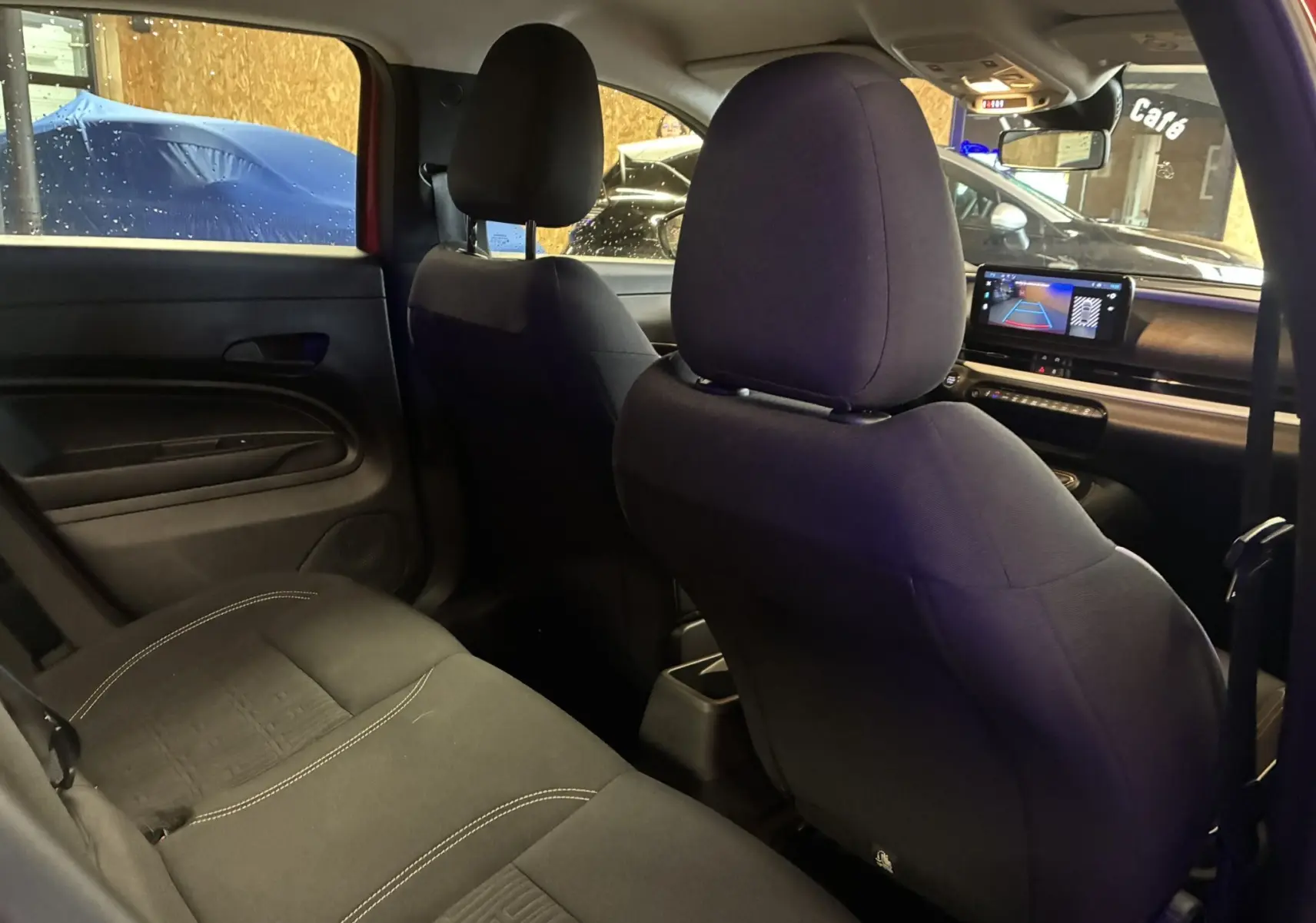 Vue intérieure arrière droite du Fiat 600 rouge 2024, sièges en tissu noir et écran tactile de recul visible au tableau de bord.