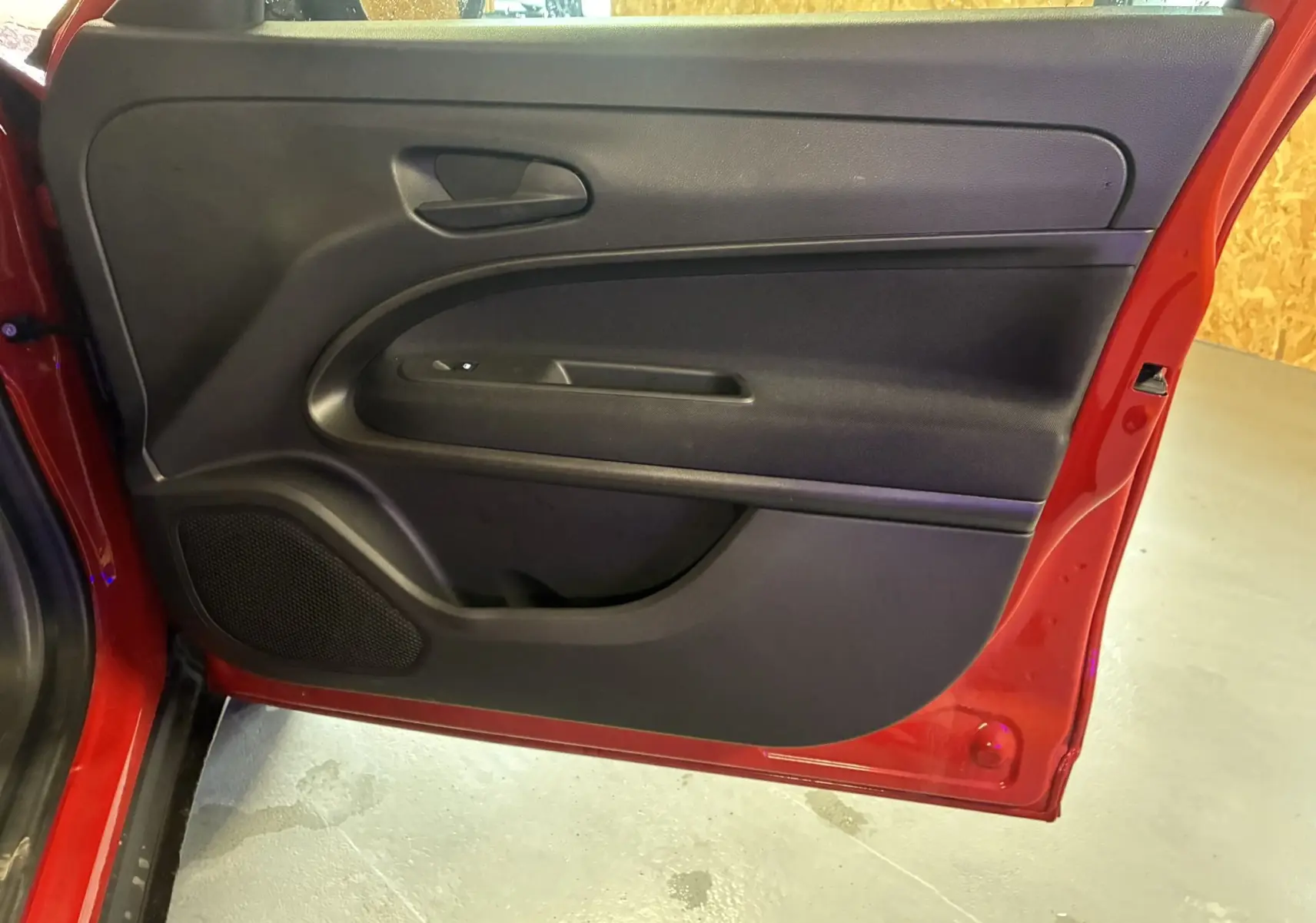 Vue intérieure de la porte arrière gauche rouge d'une FIAT 600 1.2 HYBRID 100 avec panneau noir et haut-parleur intégré.