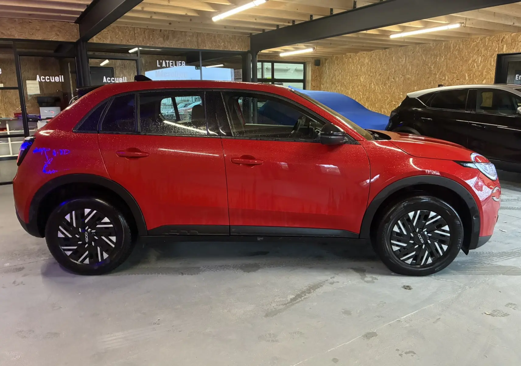 Vue de profil côté gauche d'une FIAT 600 1.2 Hybrid 2024 rouge avec jantes noires et détails noirs sur les bas de caisse.
