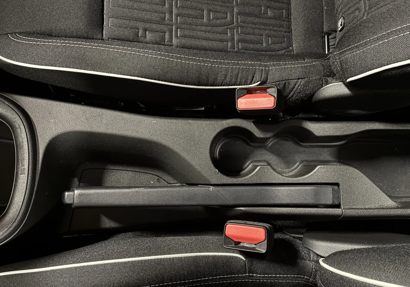 Vue plongeante sur la console centrale noire et les sièges tissu noir avec surpiqûres blanches de la FIAT 600 1.2 Hybrid rouge 2024.