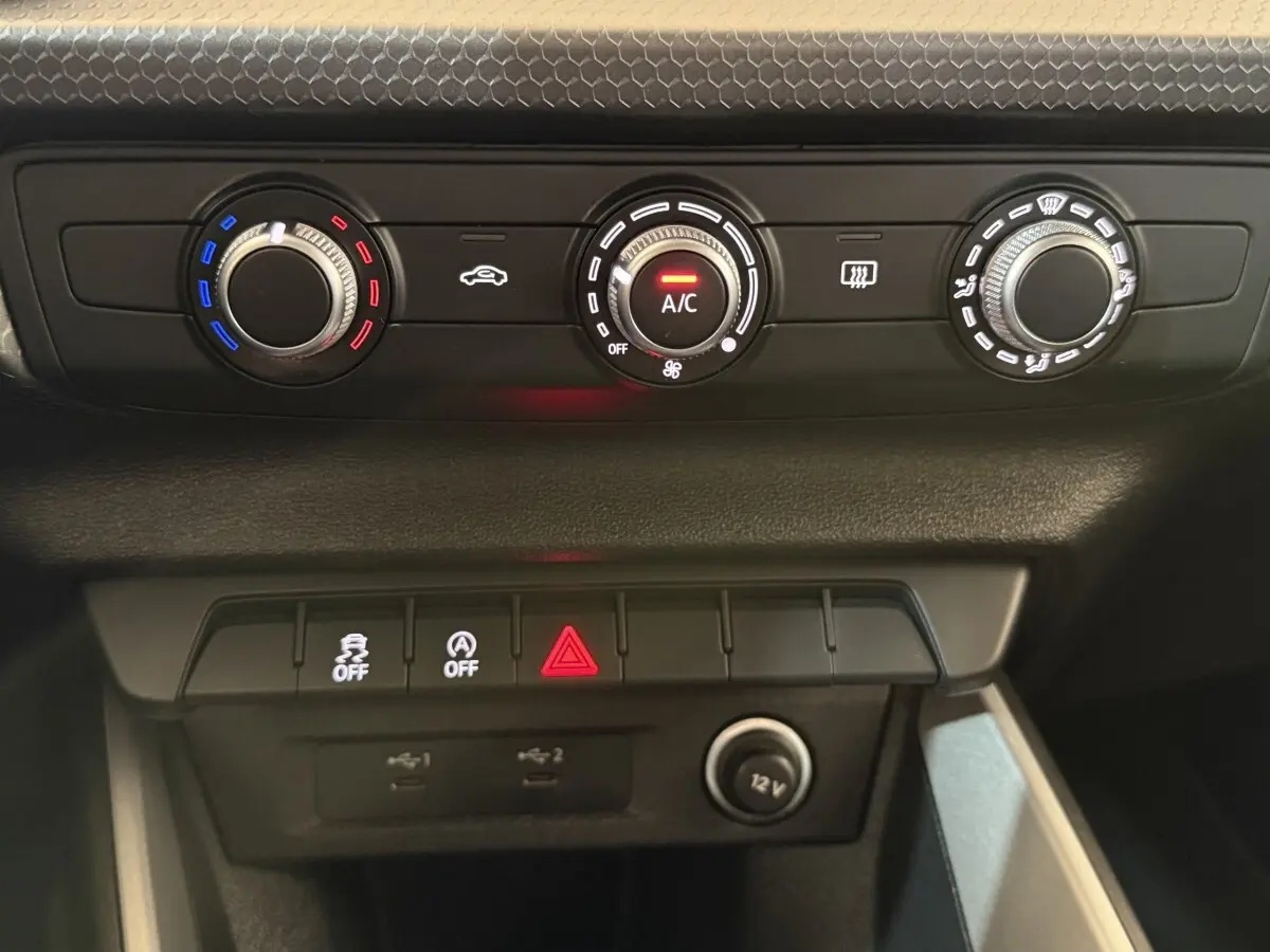 Vue rapprochée du tableau de bord de l’Audi A1 2021 noir, montrant les commandes de climatisation et boutons de sécurité.