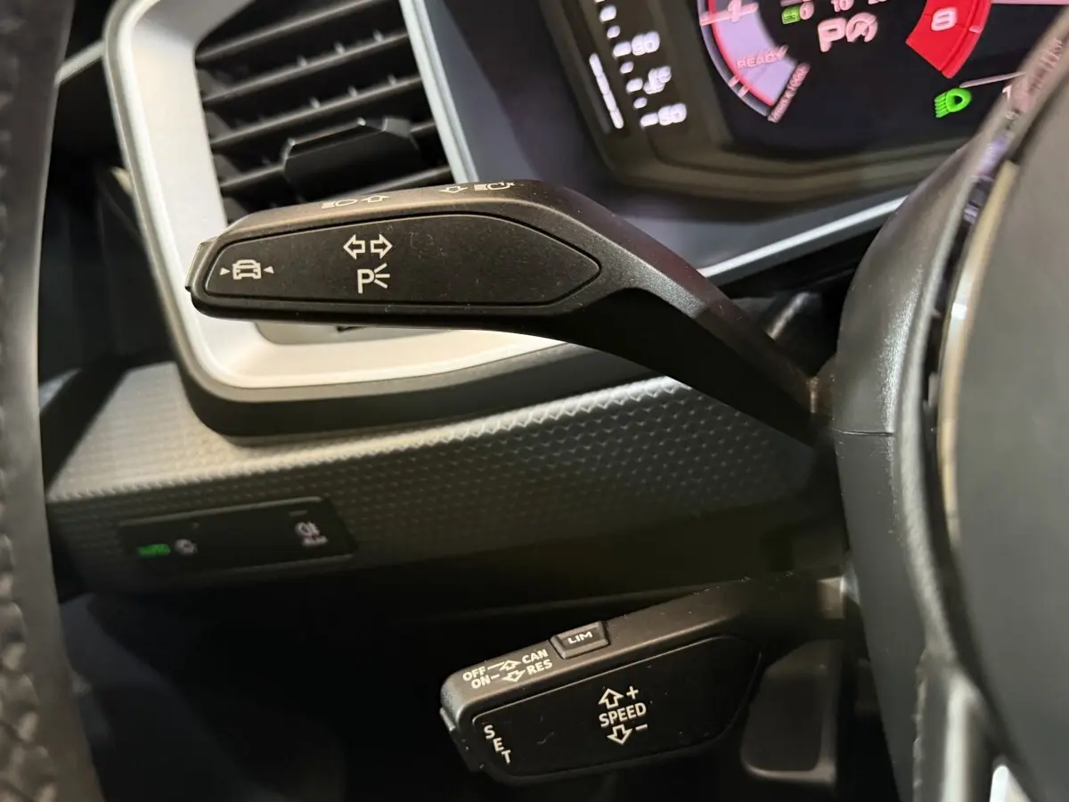 Gros plan sur les commandes au volant de l’Audi A1 noire, avec levier de clignotants et régulateur de vitesse visibles.