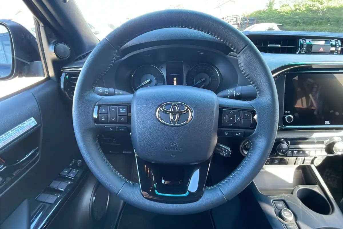 Vue intérieure centrée sur le volant en cuir noir du Toyota Hilux 4x4 2025 avec tableau de bord et commandes visibles.