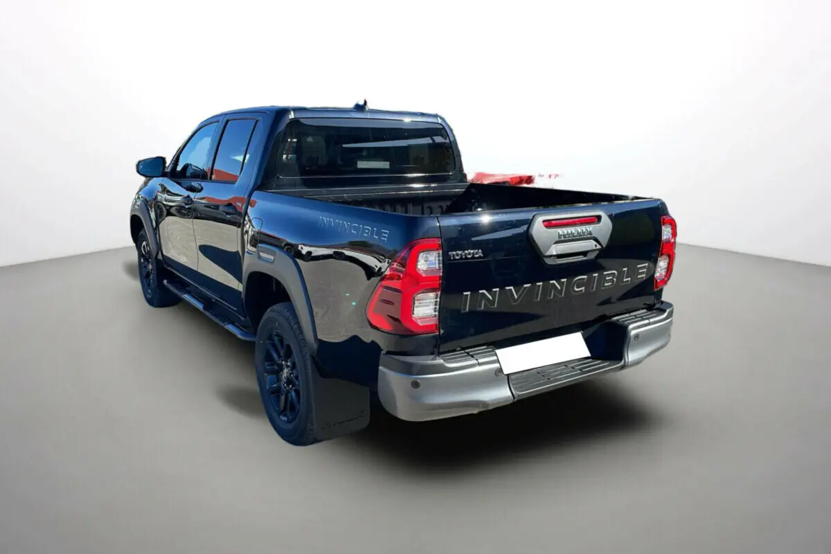 Toyota Hilux 4x4 Invincible 2025 en noir attitude, vue arrière 3/4 gauche avec benne ouverte et jantes noires.
