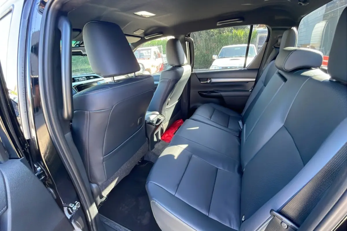 Vue intérieure arrière côté gauche du Toyota Hilux 4x4 2025 Noir Attitude avec sièges en cuir noir et espace spacieux.
