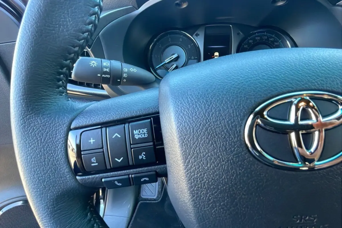 Gros plan sur le volant noir du Toyota Hilux 2025 avec commandes intégrées et tableau de bord visible en arrière-plan.