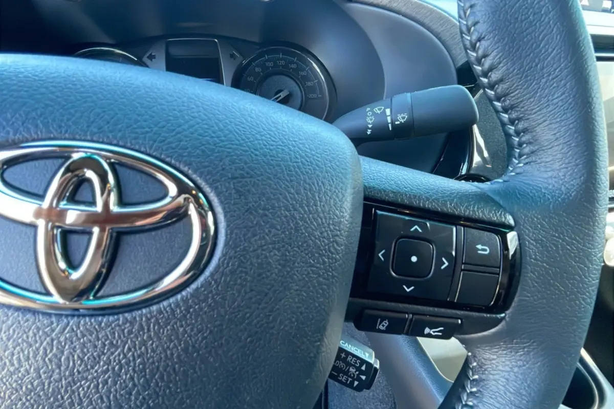 Gros plan sur le volant en cuir noir du Toyota Hilux 2025 avec commandes intégrées et logo chromé visible.