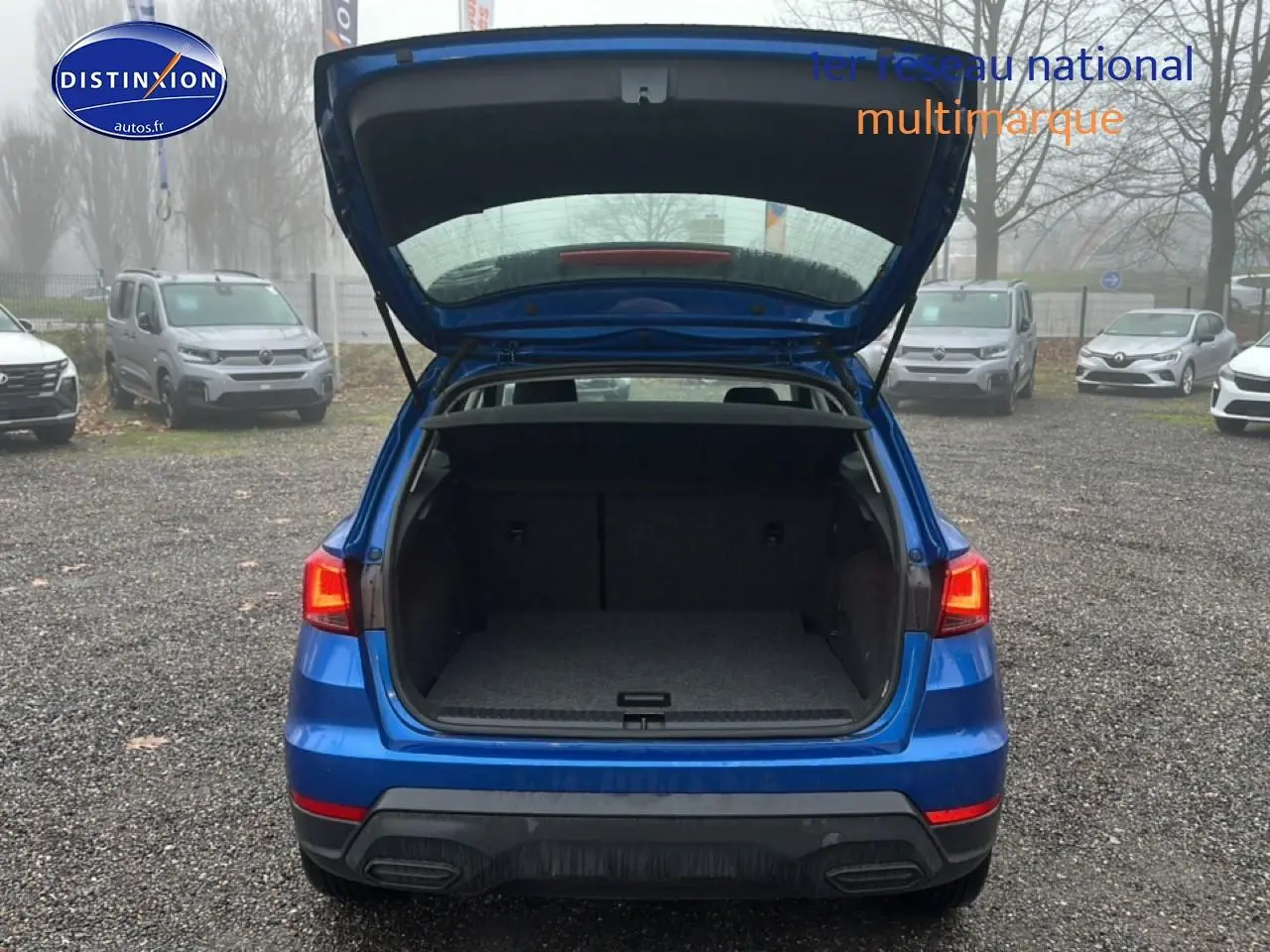 Vue arrière d’un SEAT Arona bleu saphir avec hayon ouvert montrant le coffre vide sur un parking extérieur.
