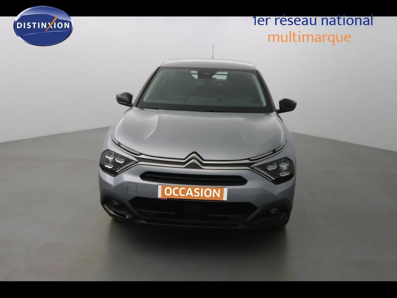Vue frontale d'une Citroën C4 gris Artense métal 2023 avec calandre distinctive et phares LED allumés.