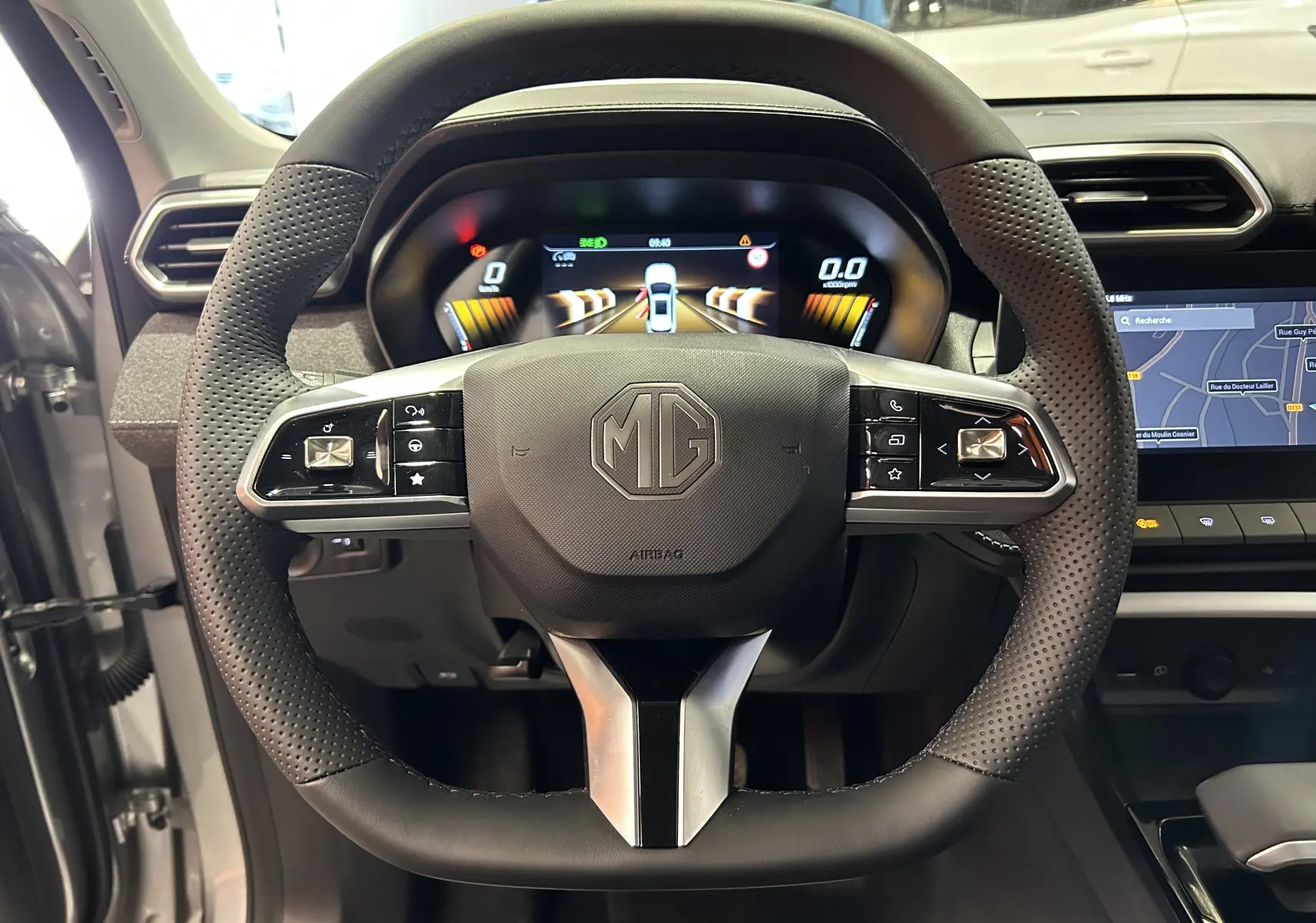 Vue intérieure centrée sur le volant perforé noir du MG ZS Cosmic Silver avec tableau de bord digital et écran GPS.