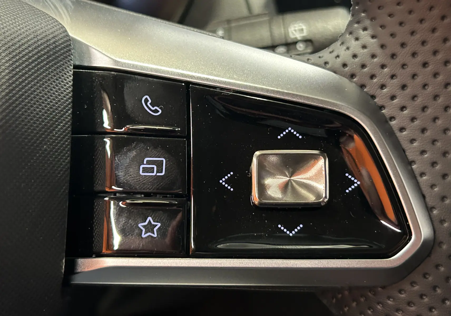 Gros plan sur les commandes noires et argentées au volant perforé du MG ZS Cosmic Silver 2025, version hybride.