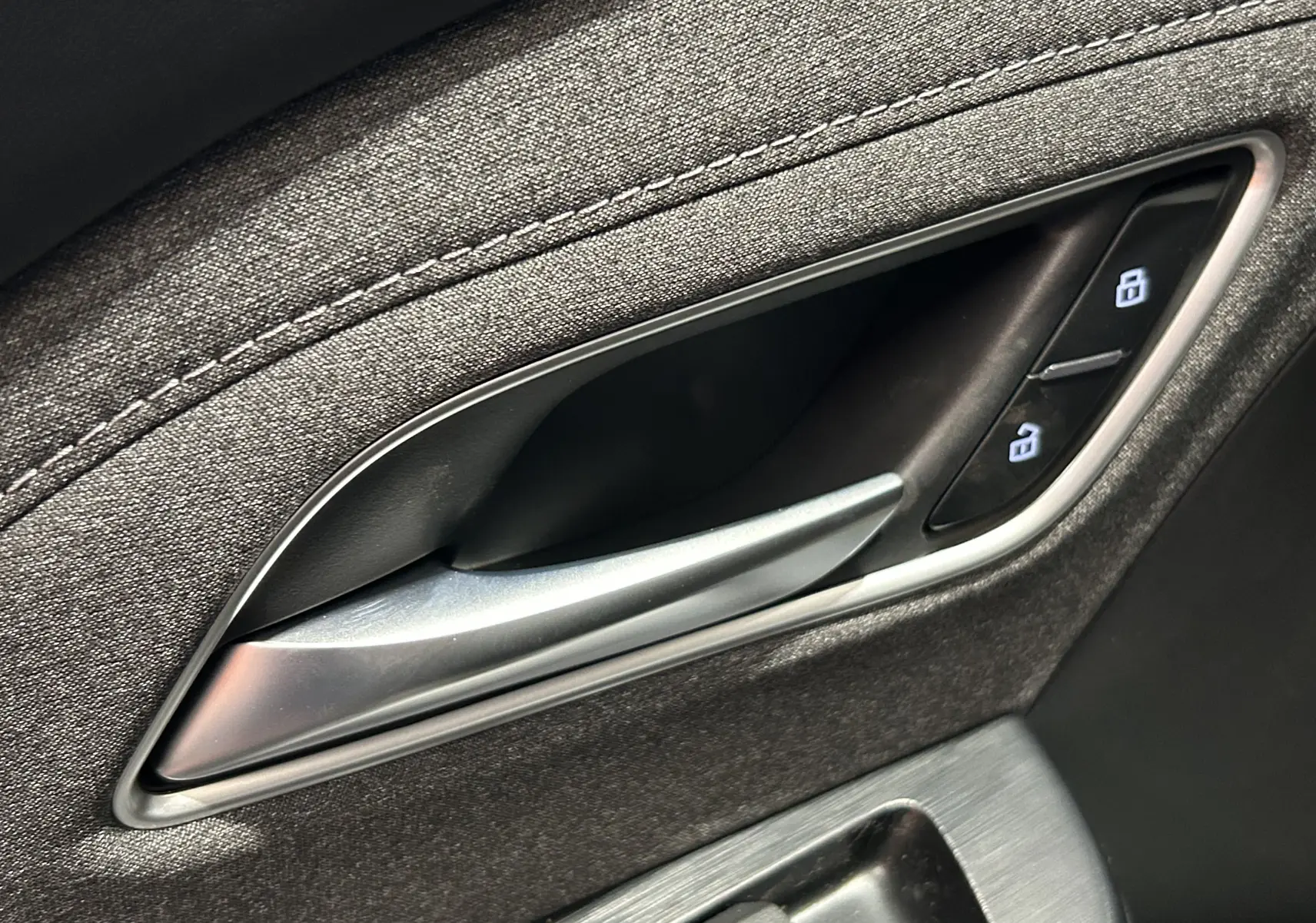 Poignée intérieure de porte côté gauche du MG ZS 2025 en tissu gris avec boutons de verrouillage éclairés.