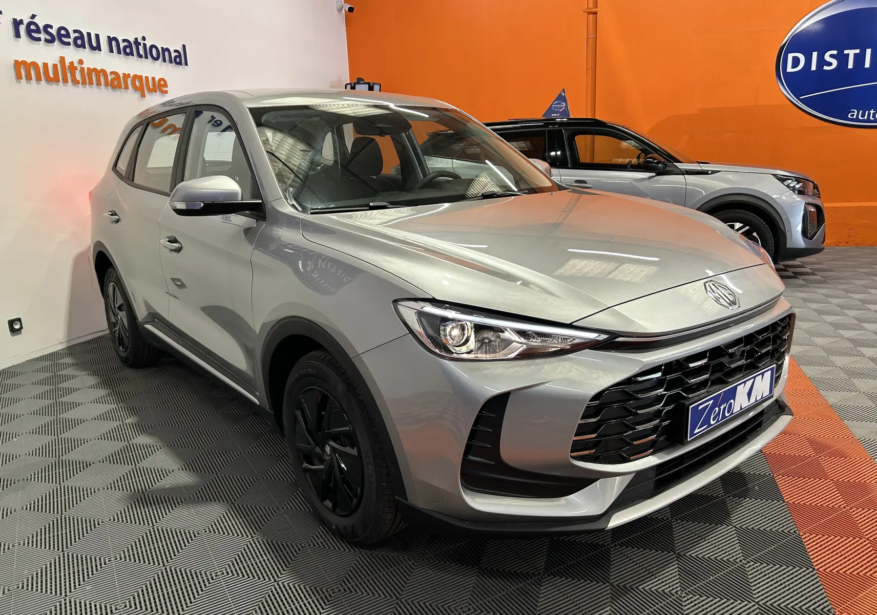 Vue 3/4 avant d’un MG ZS Cosmic Silver 2025 avec calandre noire et jantes noires dans un showroom.