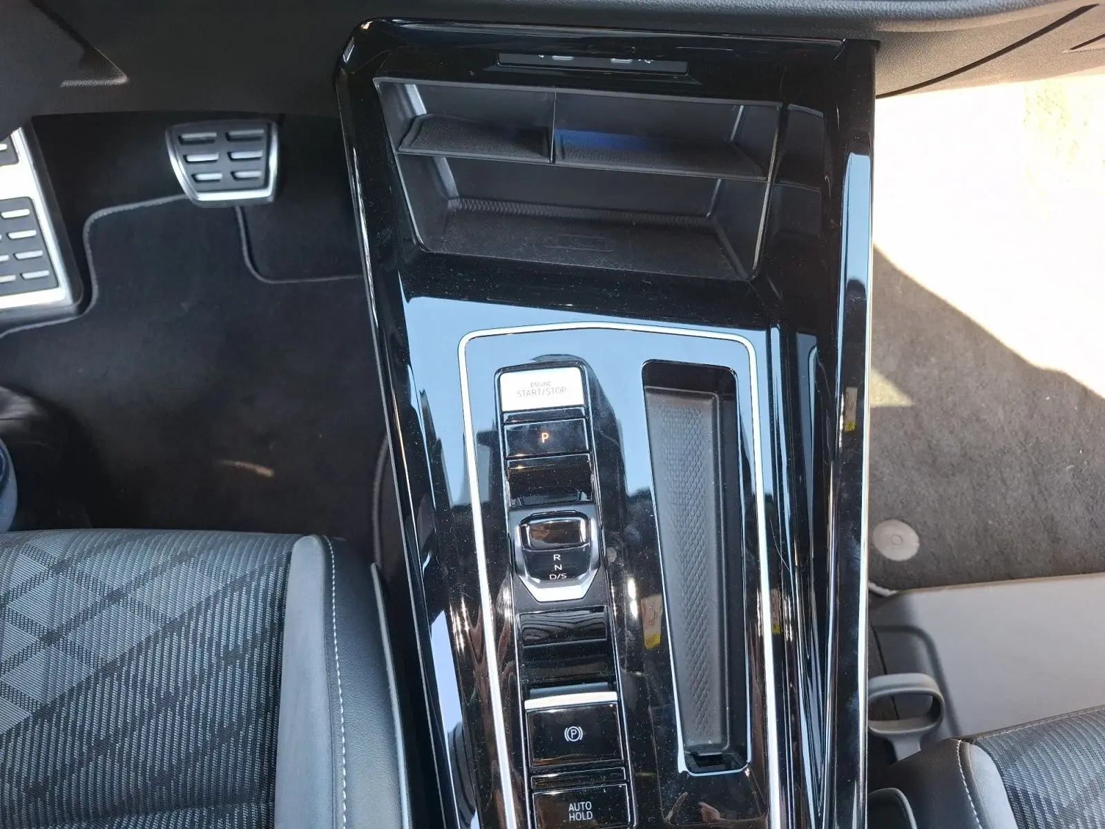 Vue plongeante sur la console centrale noire brillante de la Volkswagen Golf blanche, avec levier de vitesses DSG et bouton start/stop.