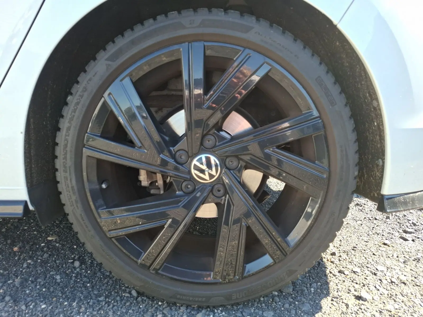 Gros plan sur la jante noire brillante côté gauche d'une Volkswagen Golf blanche 2023, avec logo VW au centre.