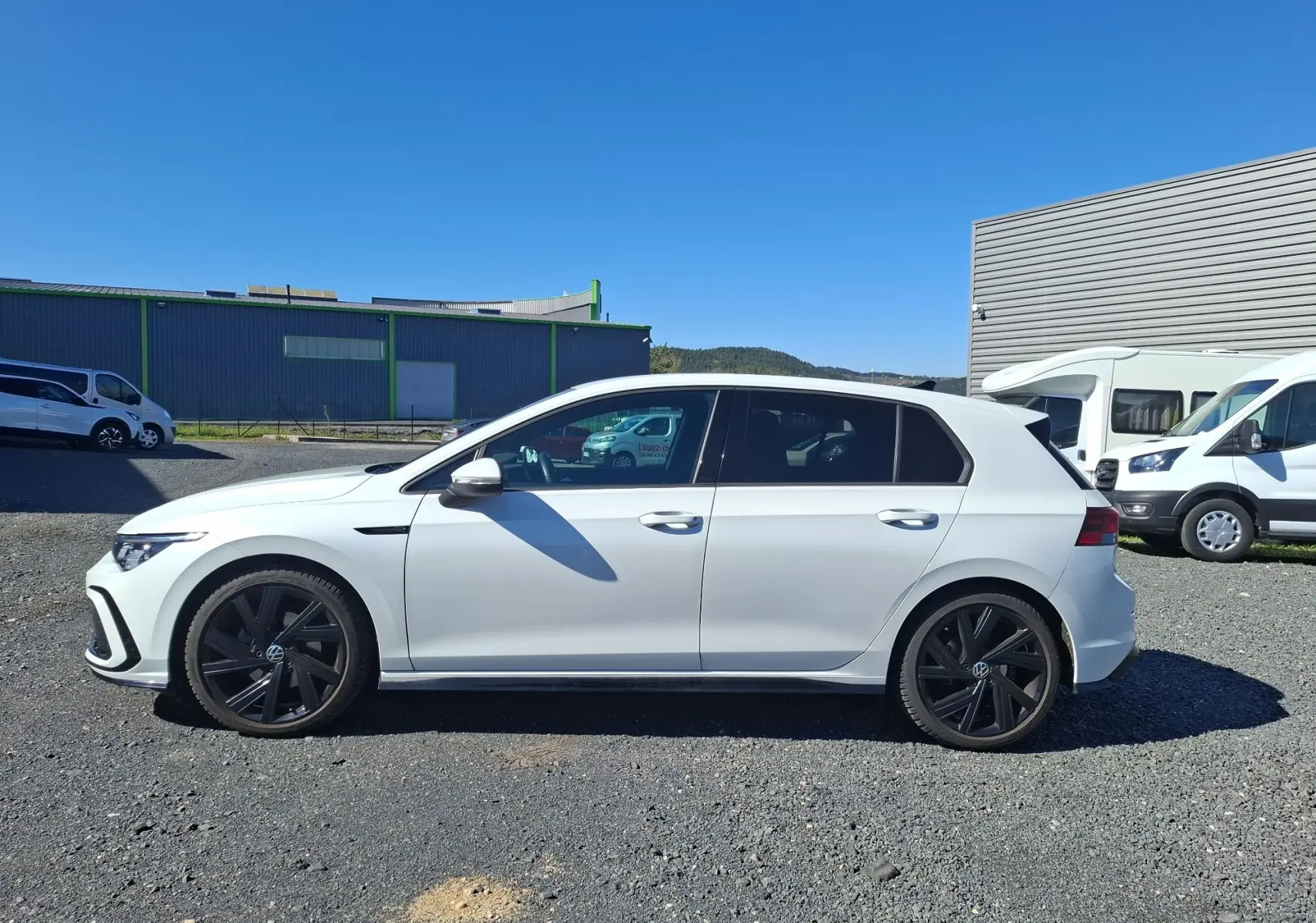 Vue de profil côté gauche d'une Volkswagen Golf blanche 2023 avec jantes noires et vitres arrière surteintées.