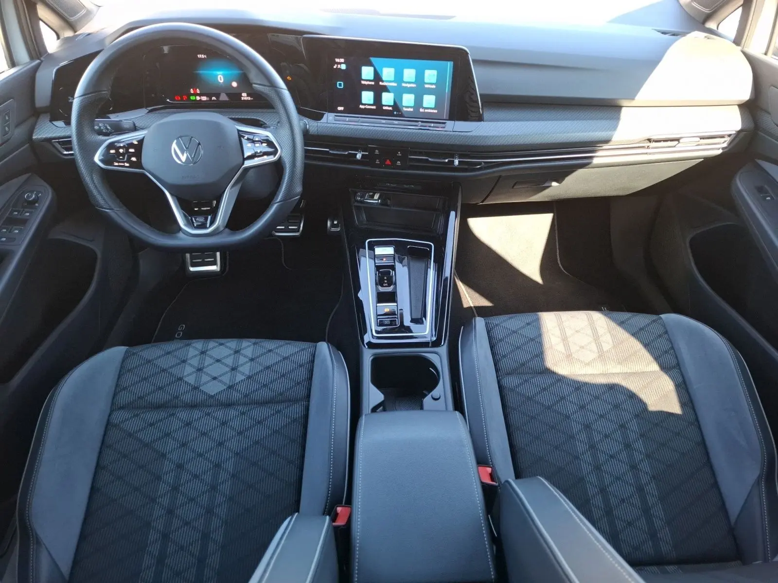 Vue intérieure avant de la Volkswagen Golf 1.5 E-TSI R-Line 2023, montrant le volant, l’écran tactile et les sièges sport noirs.
