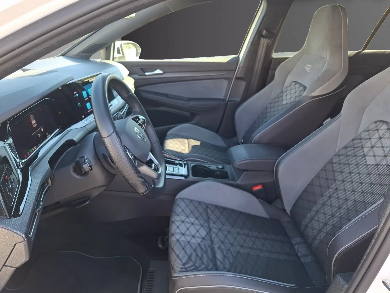 Vue intérieure côté conducteur de la Volkswagen Golf 1.5 E-TSI R-Line 2023 avec sièges sport gris et tableau de bord digital.