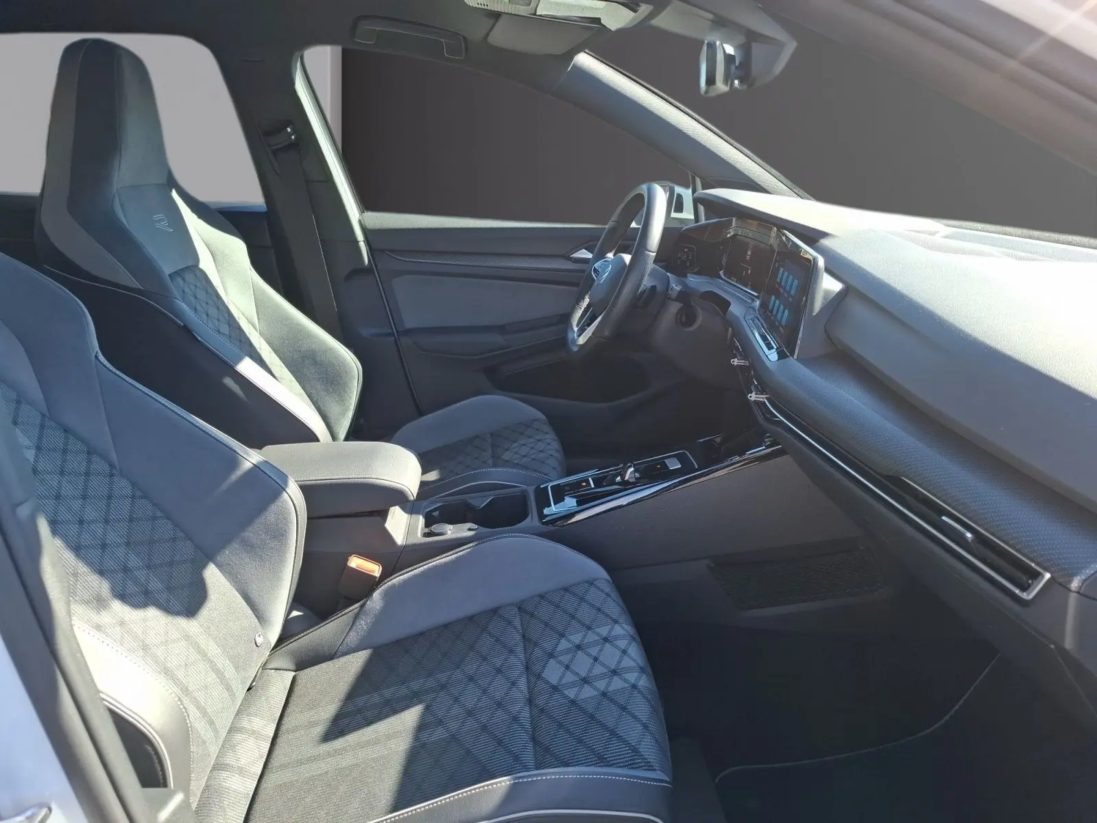 Vue intérieure côté conducteur de la Volkswagen Golf 1.5 E-TSI R-Line 2023 avec sièges sport en tissu gris et tableau de bord moderne.
