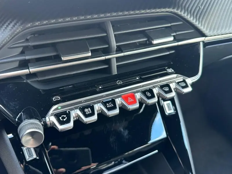 Gros plan sur la rangée de boutons chromés et noirs de la console centrale du Peugeot 2008 bleu hybride 2025.
