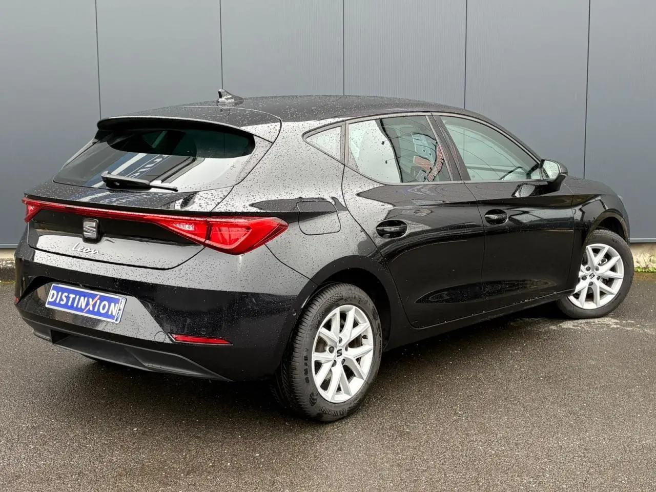 Vue 3/4 arrière droite d'une SEAT Leon 2024 noire Minuit avec jantes alliage 16 pouces sous la pluie.