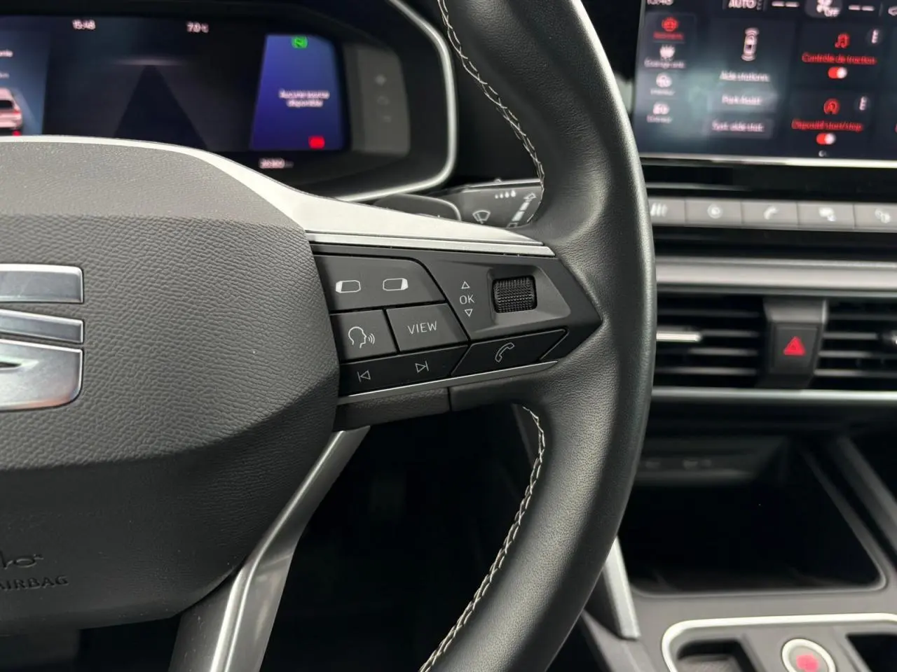 Gros plan sur le volant cuir noir de la SEAT LEON 2024 avec commandes multifonctions et combiné digital en arrière-plan.