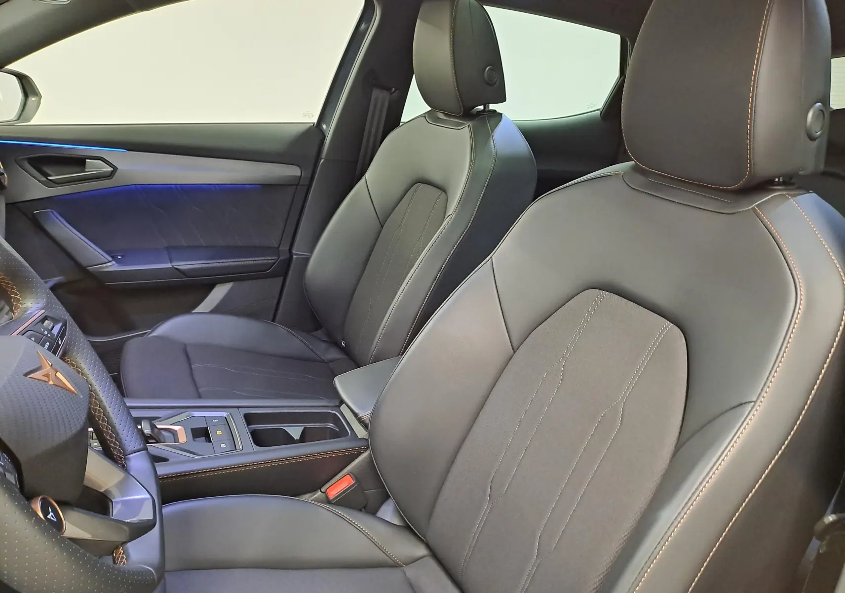 Vue intérieure côté conducteur du CUPRA Formentor 1.4 EHybrid 2025, sièges noirs avec surpiqûres cuivrées et éclairage d'ambiance bleu.