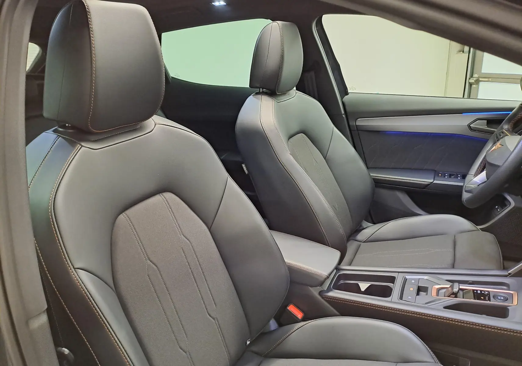 Vue intérieure côté droit montrant les sièges avant en cuir noir avec surpiqûres cuivrées et éclairage d'ambiance bleu sur la porte.