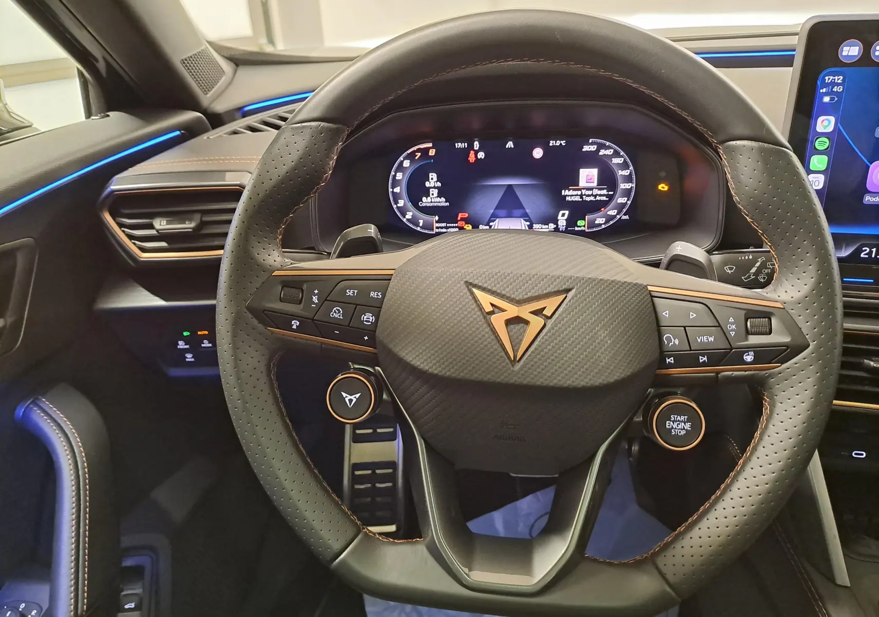 Vue intérieure centrée sur le volant cuir perforé avec logo CUPRA cuivré et tableau de bord numérique éclairé.