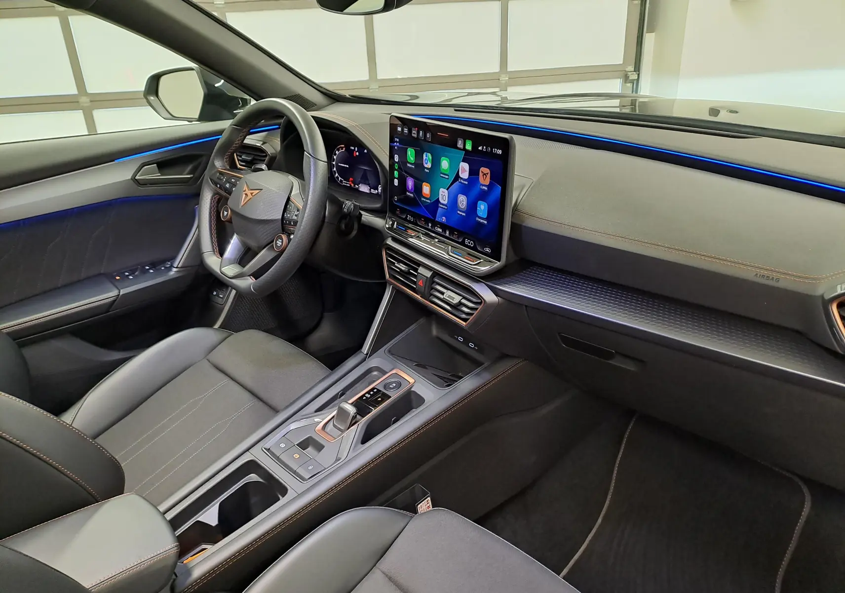 Intérieur de la CUPRA Formentor 1.4 EHybrid vu côté conducteur, avec éclairage d'ambiance bleu et écran tactile central.